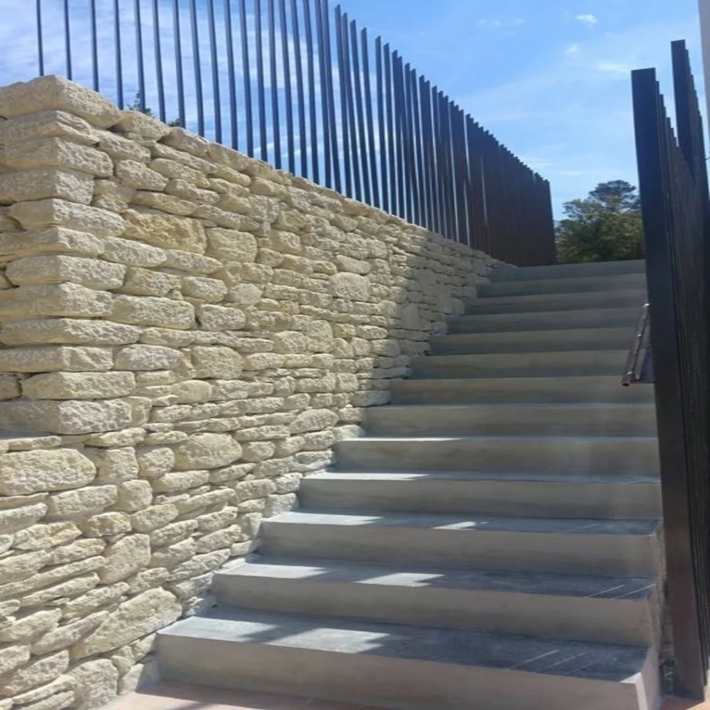 Escalier avec mu en pierre sur la gauche et garde corp en fer